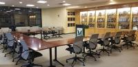 A U-shaped desk with chairs surround a podium backed by plaques in the Hall of Fame conference room