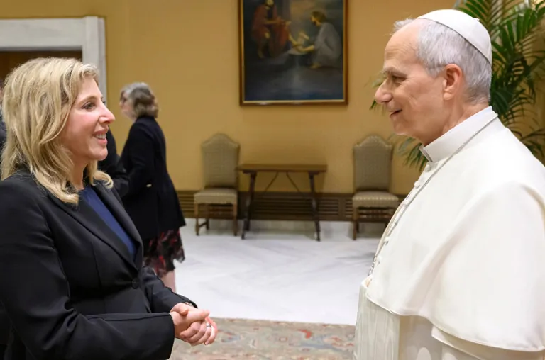 woman with blond hair in a black dress suit conversing with the Pope
