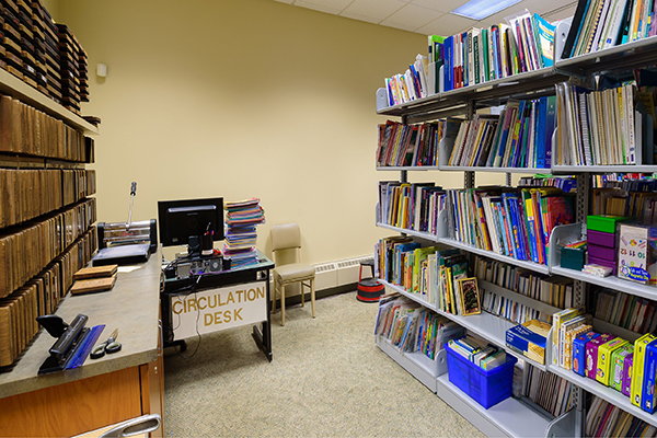 Shelves filled with books surround a desk in the Marywood curriculum lab