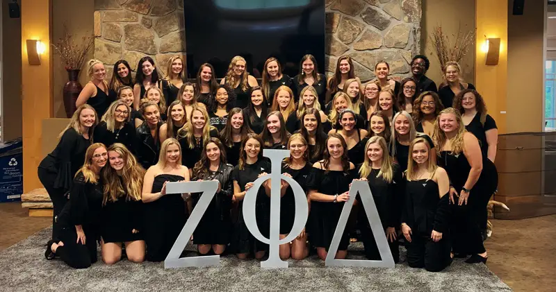 Marywood students dresseed in black dresses gather holding the Greek letters zet, phi, and delta in front