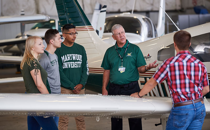 Students with professor around wing of plane