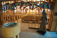 Small mosiac windows are seen from the back of a chapel along with life-sized statue of Mother Theresa Maxis