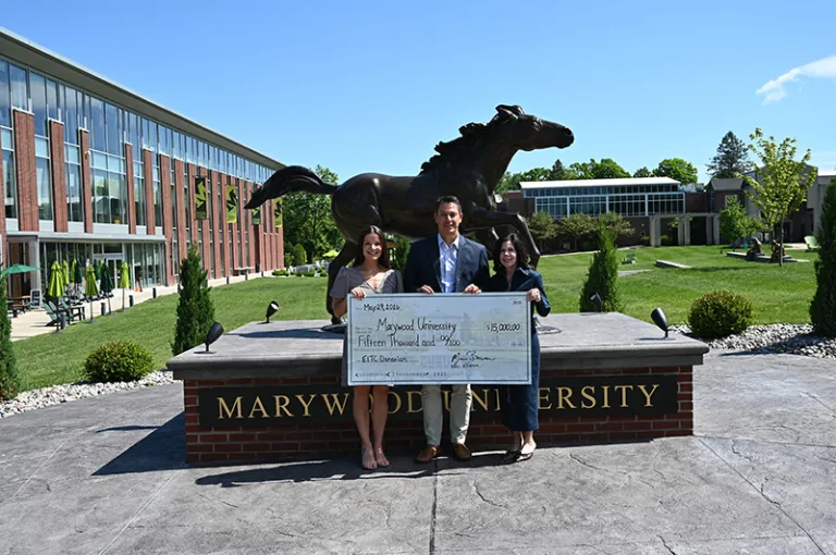 three individuals in front of a horse statue holding a check