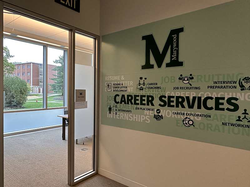 The Marywood career services office has wooden cabinets on one side and circular tables surrounded by chairs on the other