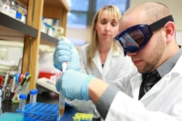 A biology student fills a test tube as his professor observes from right side