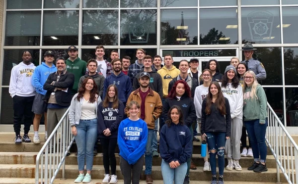 Marywood students and a state trooper taking a photo together on the stairs in front of the State Police Academy