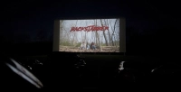 dark enviornment with a screen with the word backstabber on it Students Premiere Original Film Backstabber at Drive-In Theater