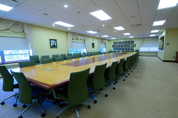 A long wooden retangular desk with chairs surrounding it in the Lynett board room