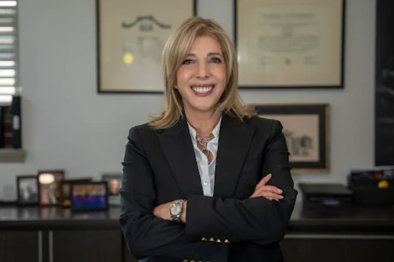 smiling blond woman in a black suit with her arms crossed