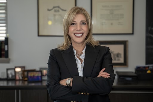 smiling blond woman in a black suit with her arms crossed