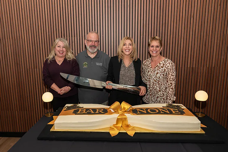 photo of four individuals with a large knife in front of a cake