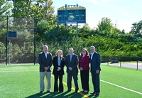 five people standing on a green athletic field in front of a blue scoreboard Peoples Security Bank & Trust Supports Marywood Athletics as Ignite the Light Scoreboard Sponsor