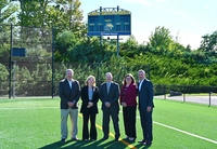 five people standing on a green athletic field in front of a blue scoreboard Peoples Security Bank & Trust Supports Marywood Athletics as Ignite the Light Scoreboard Sponsor