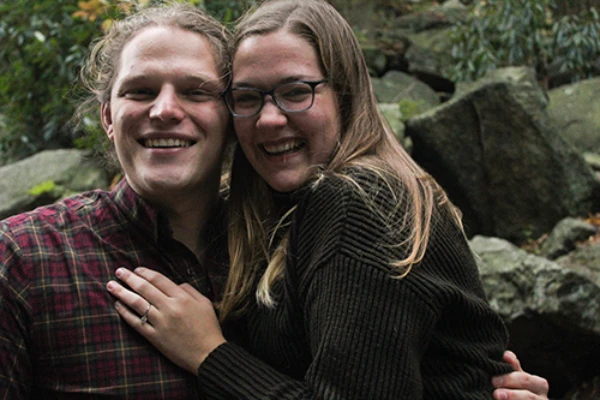 Happy couple embracing outdoors with one wearing a plaid shirt and the other in a dark sweater.