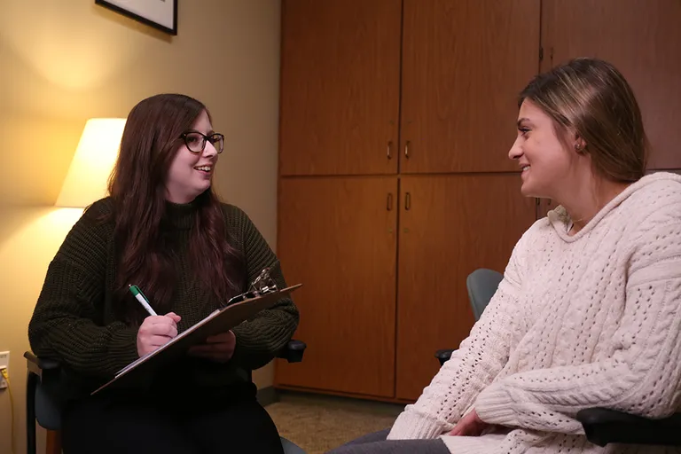 two young ladies talking, one has a clip board and a pen and paper