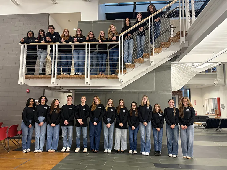 students lined up on staircase and under staircase in blue jeans and black crewnecks