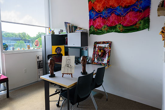 Drawings, paintings, and small sculptures of prominant African Americans, such as George Floyd, cover a L-shaped desk