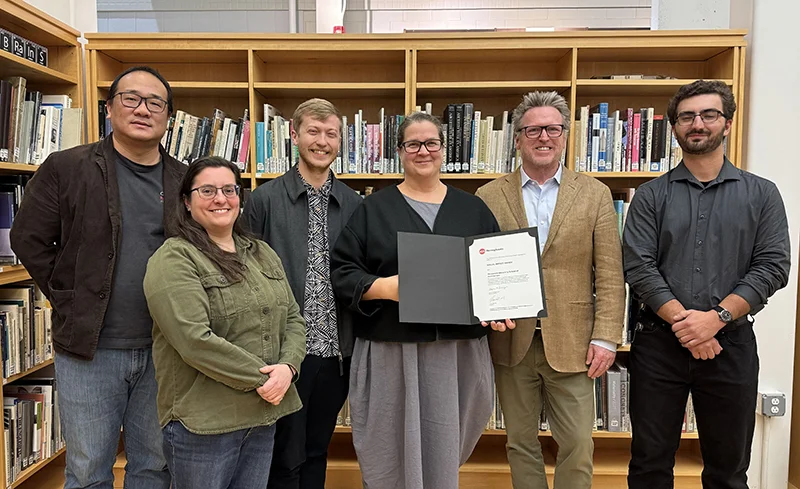 A group of men and women standing in front of a bookshelf with one woman holding an award certificate AIA Pennsylvania Honors School of Architecture with 2025 Social Impact Award