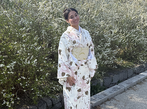 woman dressed in komoto standing in front of bushes smiling