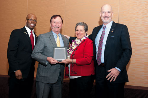 a group picture of several people with one person in the middle holding an award plaque