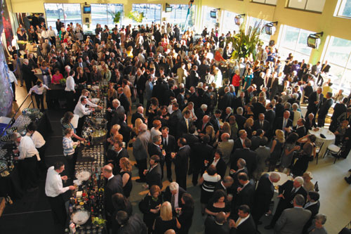 a large mass of people walking around an enclosed room. Bartenders line the left wall.