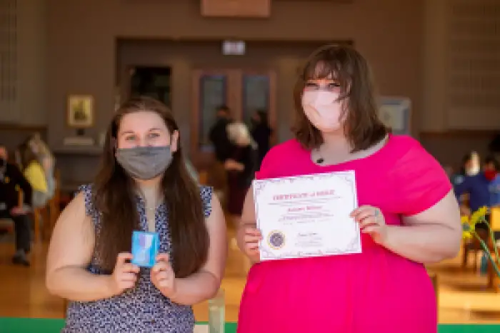 Two people showing off their respective awards, a medal and a certificate