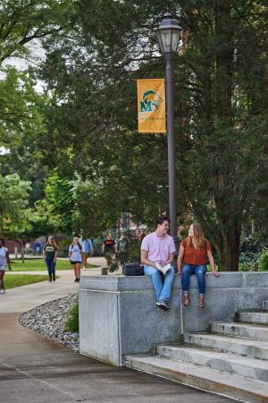 two students sit on liberal arts steps near pacers flag pole Master's in Higher Education Program Ranks Among Top