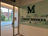 The Marywood career services office has wooden cabinets on one side and circular tables surrounded by chairs on the other