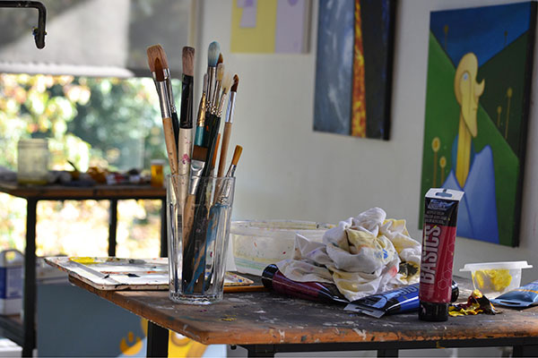 Marywood's Art Studio with a table with used art supplies and paintings on the wall