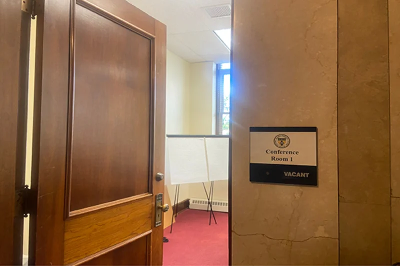 A wooden door cracked upon to reveal part of a conference room with a red carpet