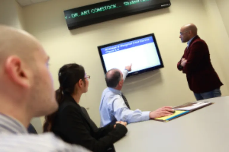 Three business students with professor point to screen and stock market ticker