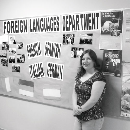 a black and white photo of Rebecca Ann Schwalb standing in front of the Foreign Languages Department bulletin board.