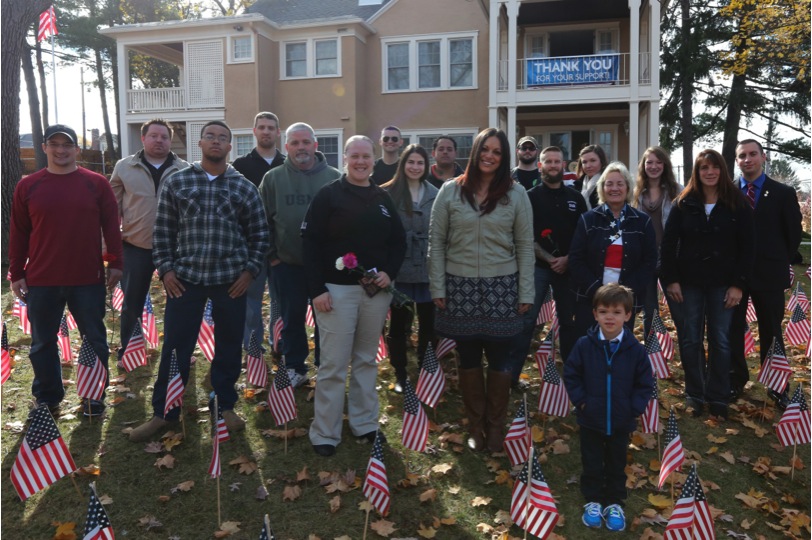 a group of people gathered for a picture looking toward the camera with miniature American flags planted around their feet.